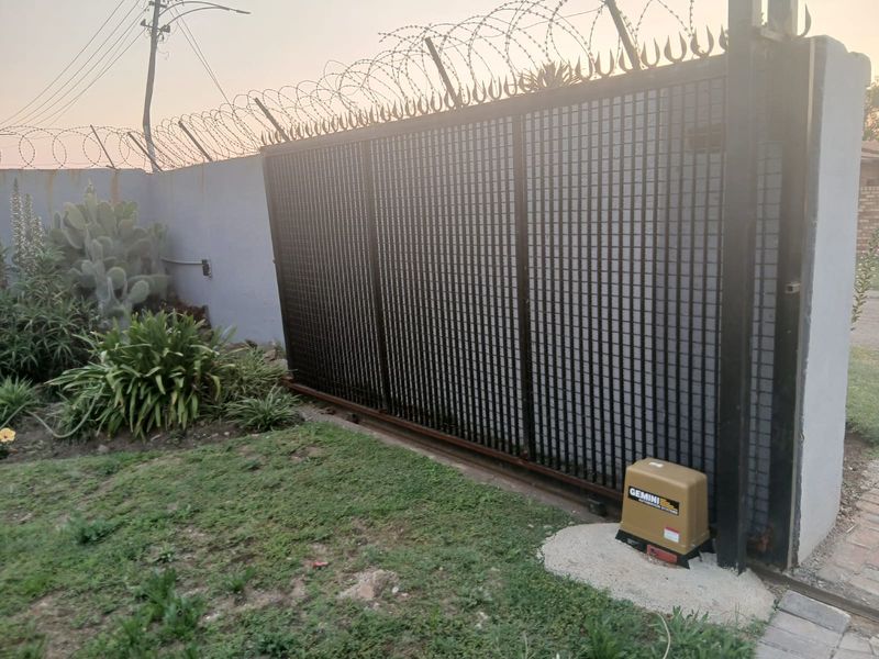 Front entrance featuring a secure sliding gate with an automated motor, perimeter walling, and installed razor wire for enhanced security.
