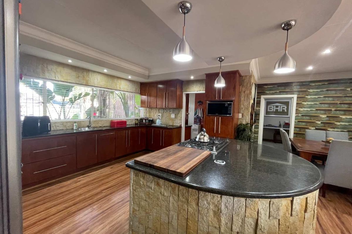 Spacious kitchen featuring a large island with granite countertops, gas hob, ample wooden cabinetry, and decorative stone cladding accents.