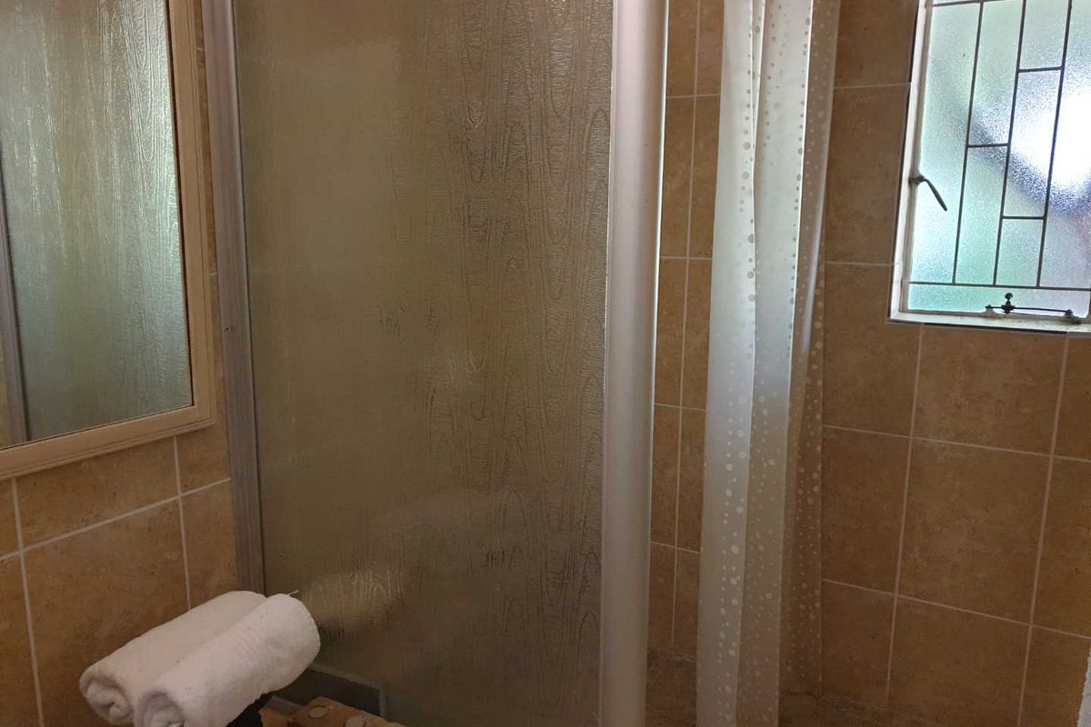 A dated bathroom featuring a shower enclosure with a glass door, tiled walls, and a window with security bars.