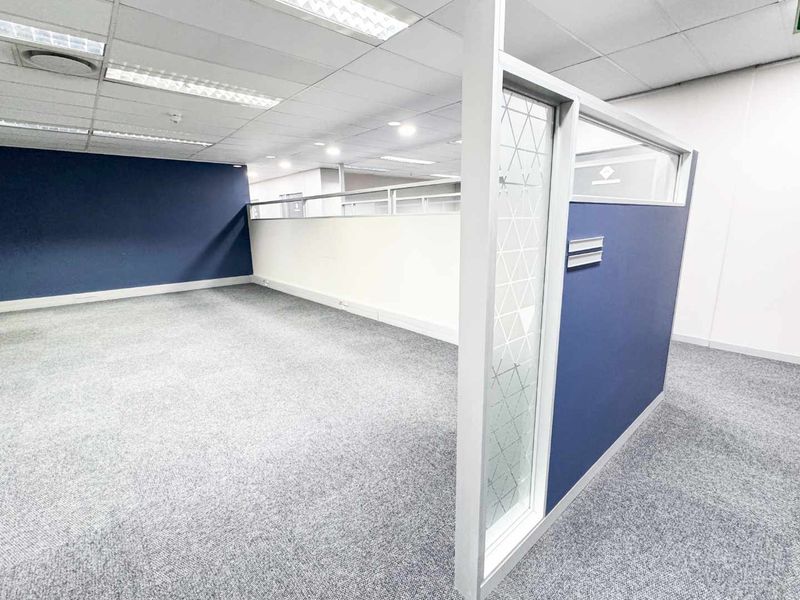 A clean, vacant office space featuring modern partition walls, suspended ceilings with recessed lighting, and neutral carpeting, ready for professional use.