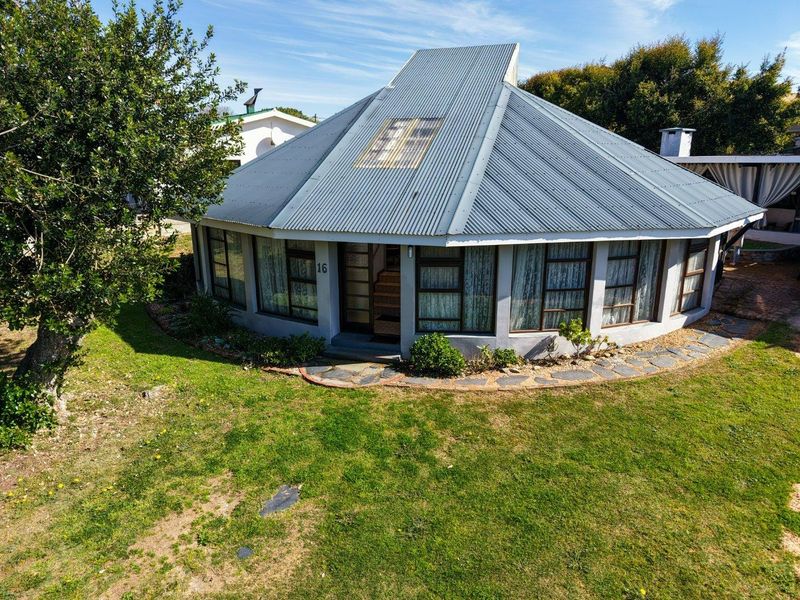 A unique circular-style house featuring a corrugated metal roof, large windows, and a surrounding garden with a stone-paved walkway.