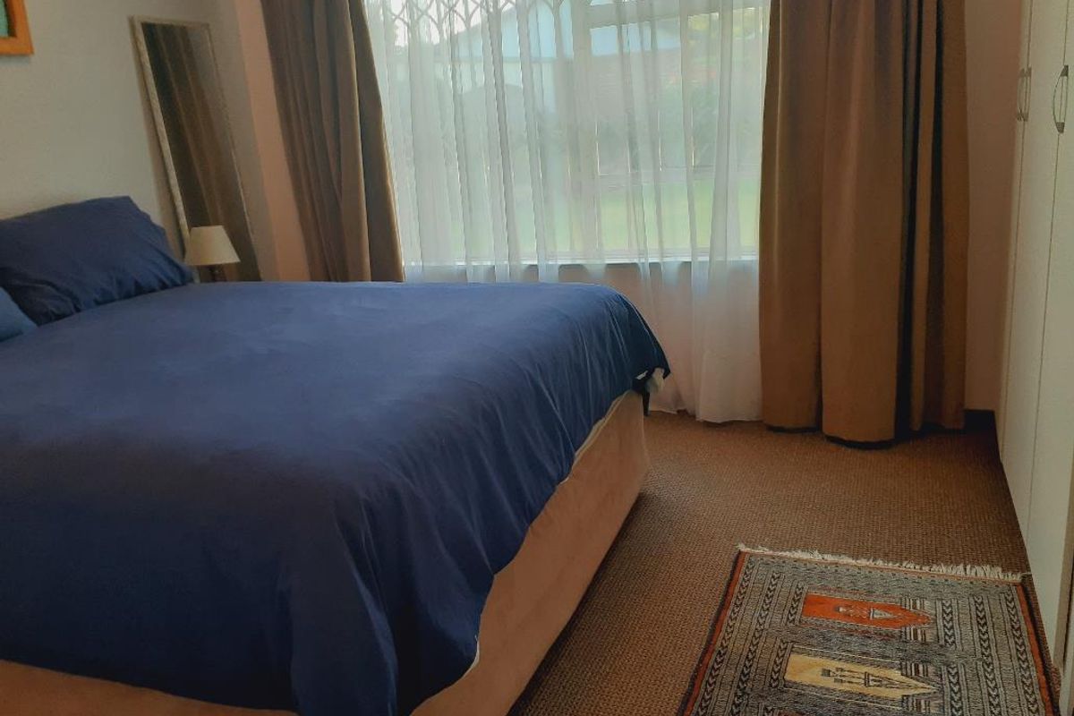 A bedroom featuring built-in cupboards and large windows with curtains, providing natural light and a view of the exterior.