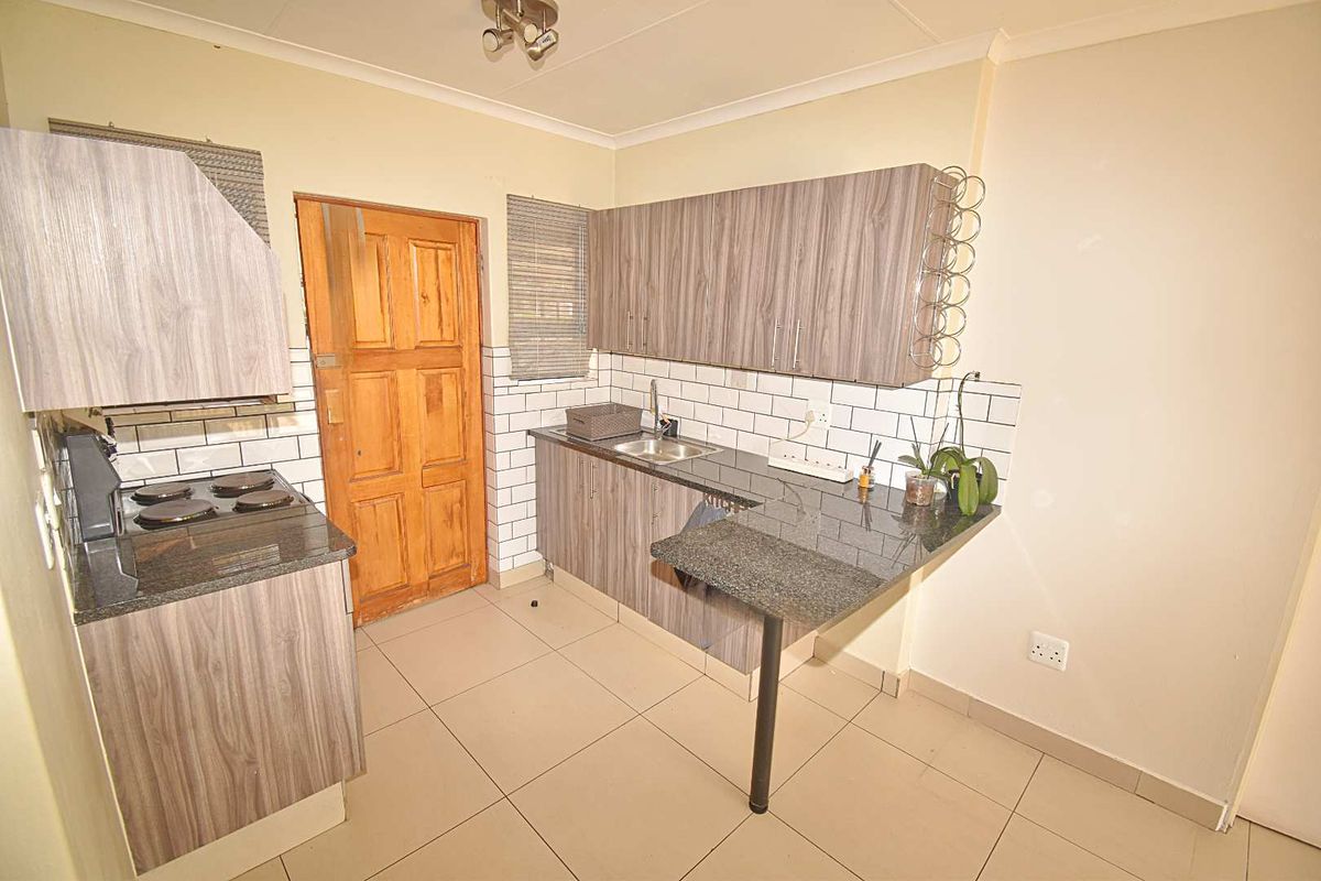 Compact kitchen featuring wood-grain cabinetry, granite countertops, subway tile backsplash, and a built-in electric hob.
