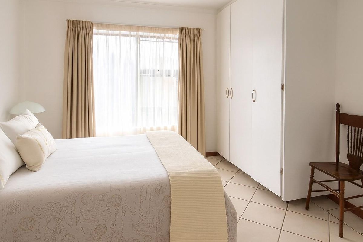 A bright bedroom featuring neutral tiled flooring and built-in floor-to-ceiling wardrobes, offering a clean and functional living space.