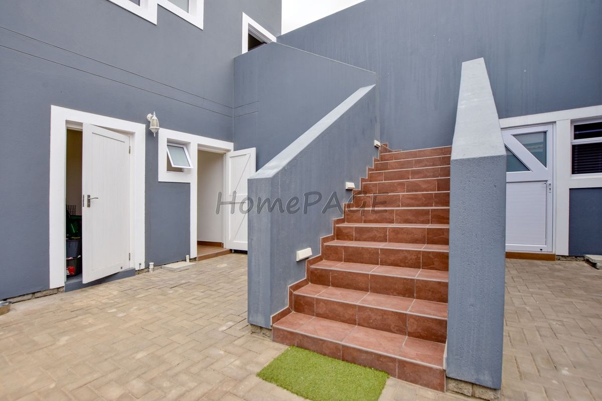 A paved rear courtyard featuring a tiled staircase leading to an upper level, complemented by modern grey exterior walls and secure access doors.