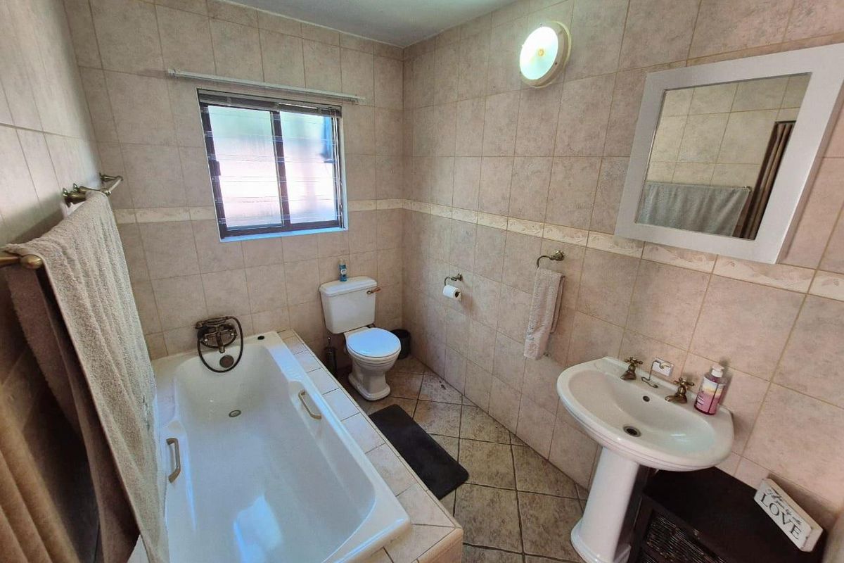 A functional bathroom featuring a built-in bathtub, pedestal basin, toilet, and full-height wall tiling.