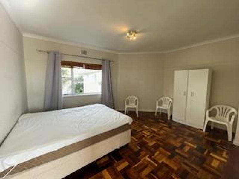 A spacious bedroom featuring classic parquet flooring, neutral walls, and a ceiling light fixture, offering a clean and functional living space.