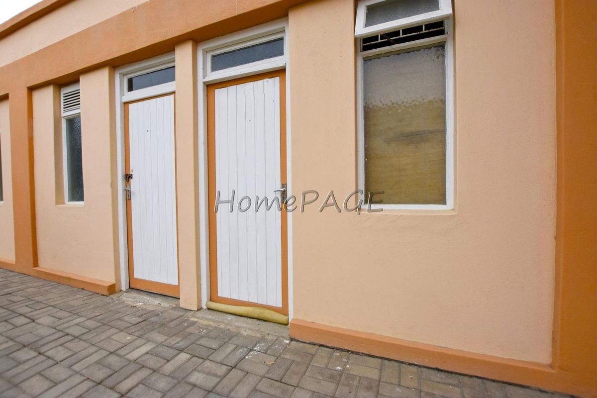Exterior view of the rear building facade featuring paved walkway access, timber doors with transom windows, and standard casement windows.