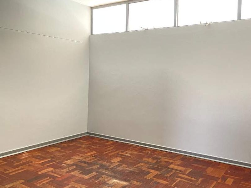 An empty bedroom featuring original parquet flooring and high-level clerestory windows, offering a blank canvas for renovation.