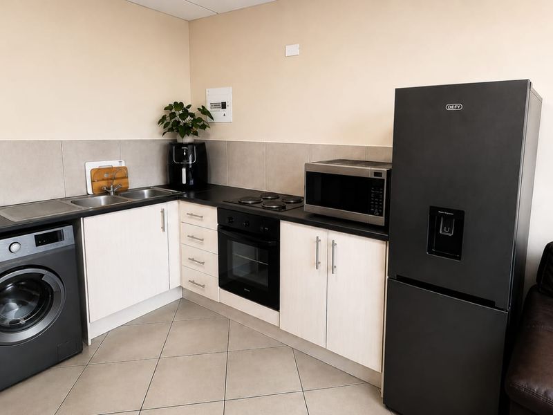 A functional kitchen featuring light-toned cabinetry, dark laminate countertops, a built-in oven with electric hob, and tiled flooring.
