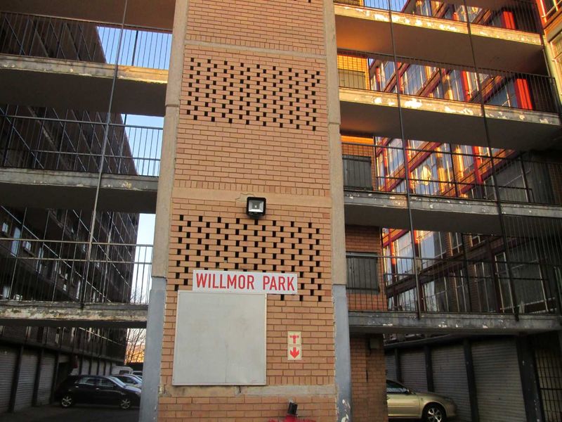 Exterior view of the Willmor Park apartment complex, featuring brick facade, external stairwells, and covered parking facilities.