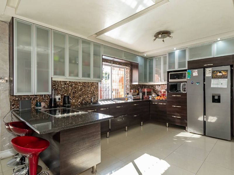 Modern kitchen featuring dark wood cabinetry, granite countertops, mosaic tile backsplash, and integrated appliances with ample storage and a breakfast bar area.