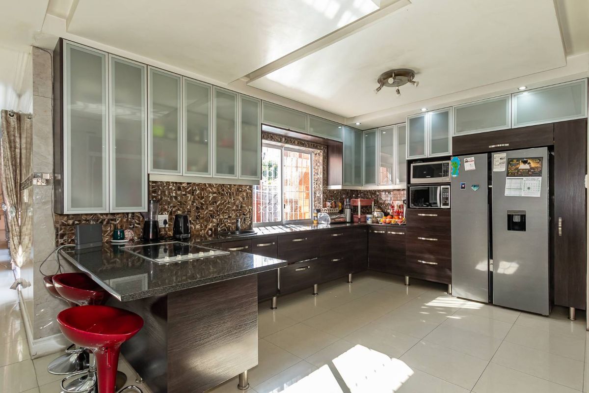 Modern kitchen featuring dark wood cabinetry, granite countertops, mosaic tile backsplash, and integrated appliances with ample storage and a breakfast bar area.