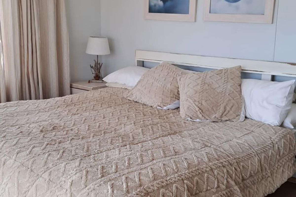A well-lit bedroom featuring neutral wall tones, wood-look flooring, and floor-to-ceiling curtains.