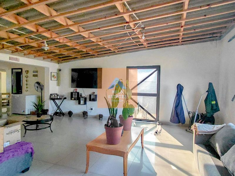 Open-plan living area featuring tiled floors and an exposed timber rafter ceiling, offering a spacious layout with direct access to the exterior.