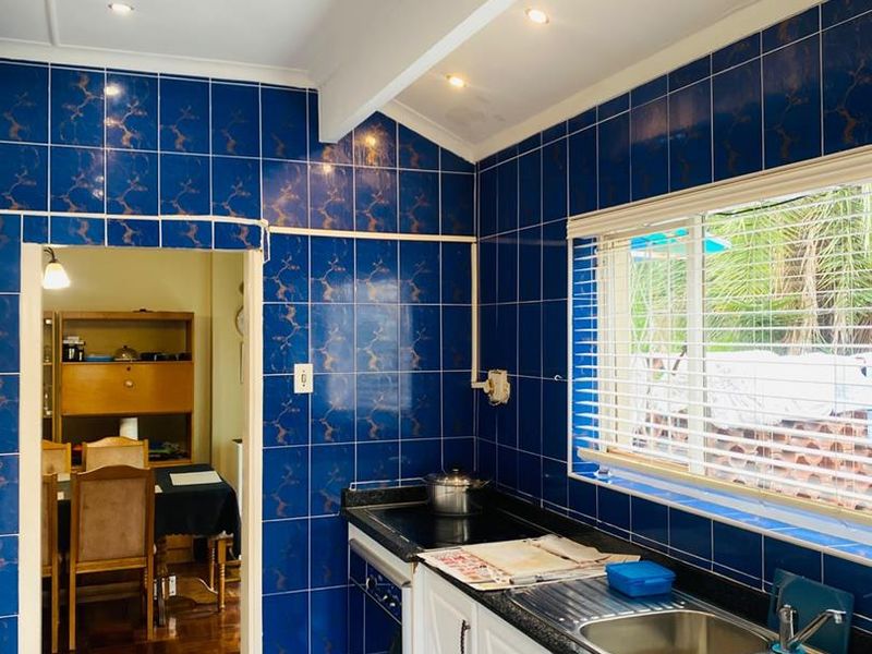 A functional kitchen featuring blue tiled walls and floors, white cabinetry, a double bowl stainless steel sink, and a built-in hob.