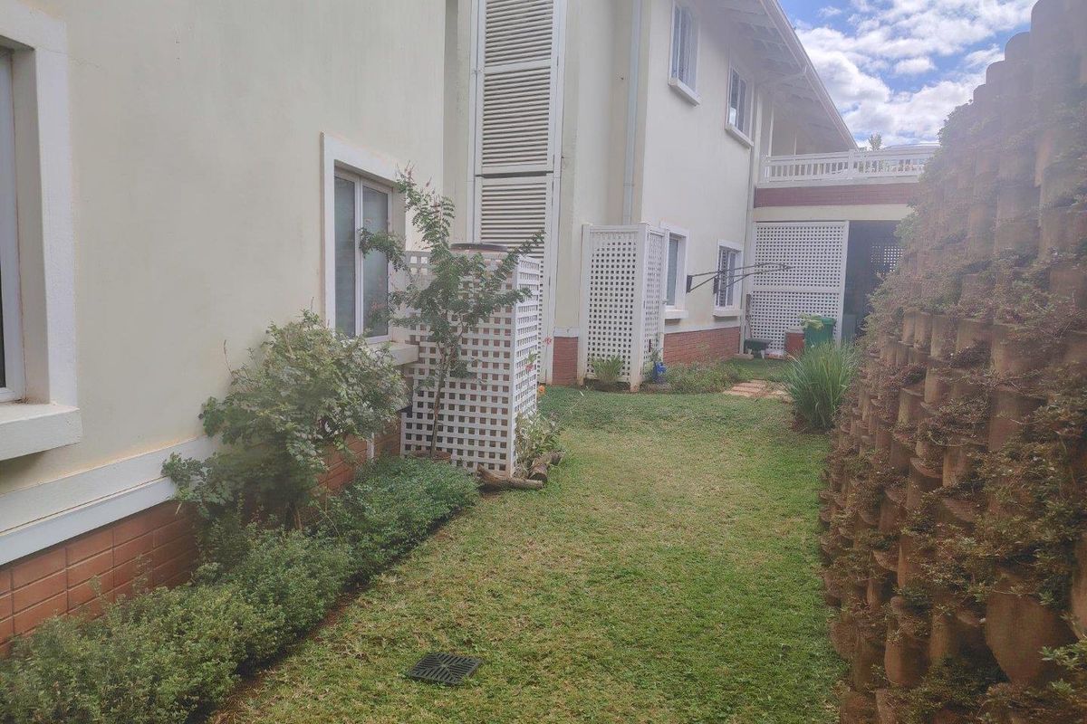 A side garden area featuring a grass lawn, a tiered retaining wall, and white lattice privacy screens along the building exterior.