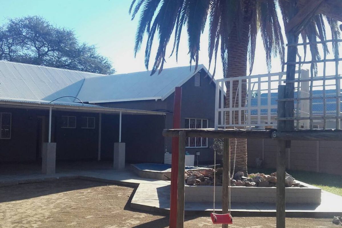 Rear view of the property featuring a covered patio area, a paved section, and a garden space with a large palm tree.