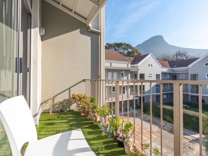 A well-maintained balcony featuring artificial grass flooring, a metal balustrade, and views of the surrounding apartment complex and mountain.