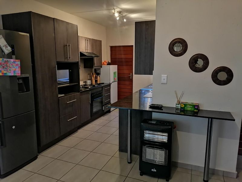 Modern kitchen featuring dark wood cabinetry, granite countertops, a breakfast bar, and built-in appliances, finished with neutral floor tiles.