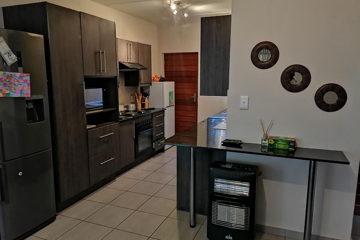 Modern kitchen featuring dark wood cabinetry, granite countertops, a breakfast bar, and built-in appliances, finished with neutral floor tiles.