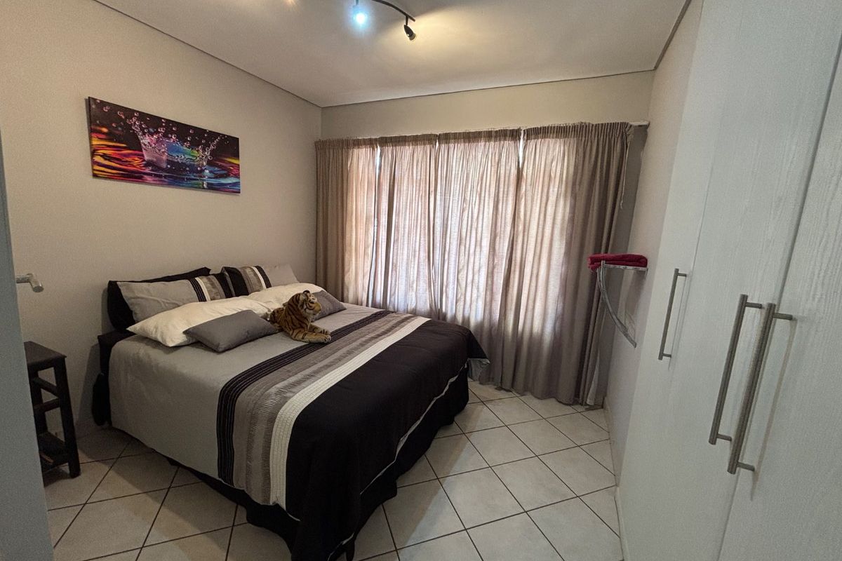 A functional bedroom featuring tiled flooring, a built-in wardrobe, and modern track lighting, offering a clean and practical living space.