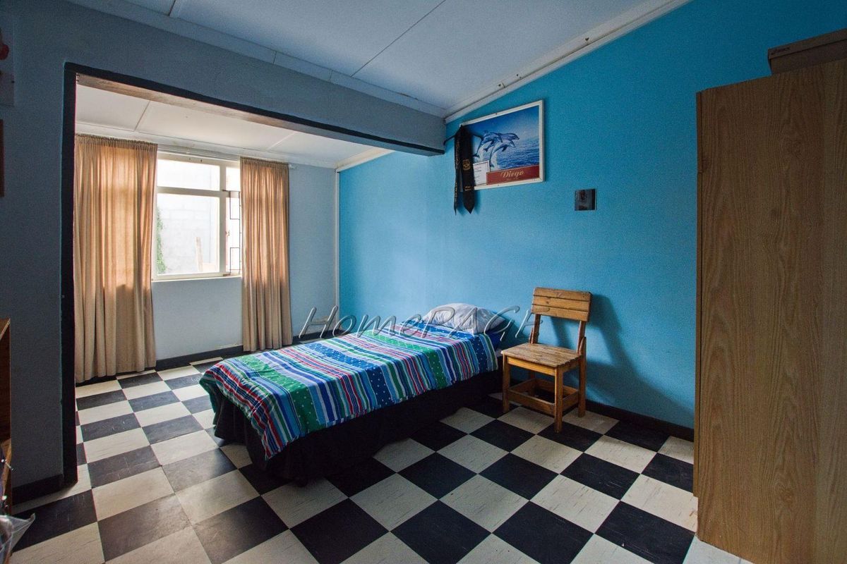 A bedroom featuring checkered floor tiles, blue painted walls, and a window with curtains.