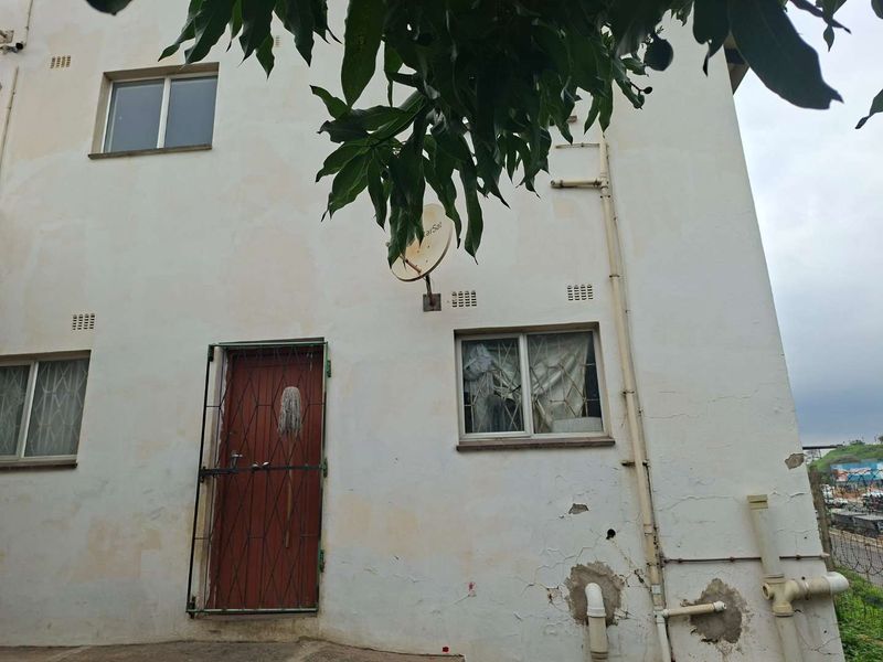 Rear exterior view of the property showing weathered plaster, security gate, and external plumbing fixtures.