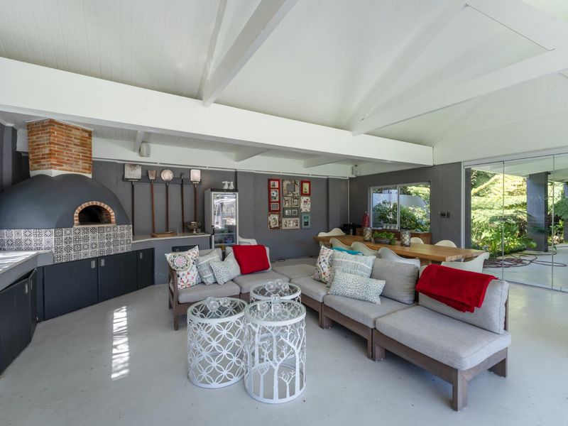 Spacious covered patio featuring a built-in pizza oven, exposed beam ceiling, and large sliding glass doors opening to the garden.