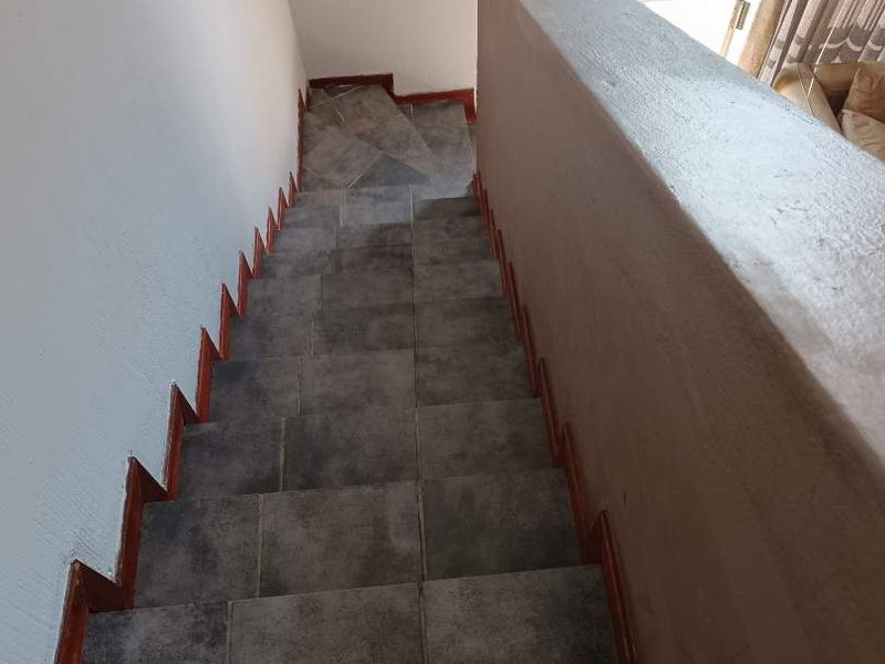 A staircase featuring dark grey floor tiles and a solid plastered balustrade, leading down towards a sliding glass door with garden access.