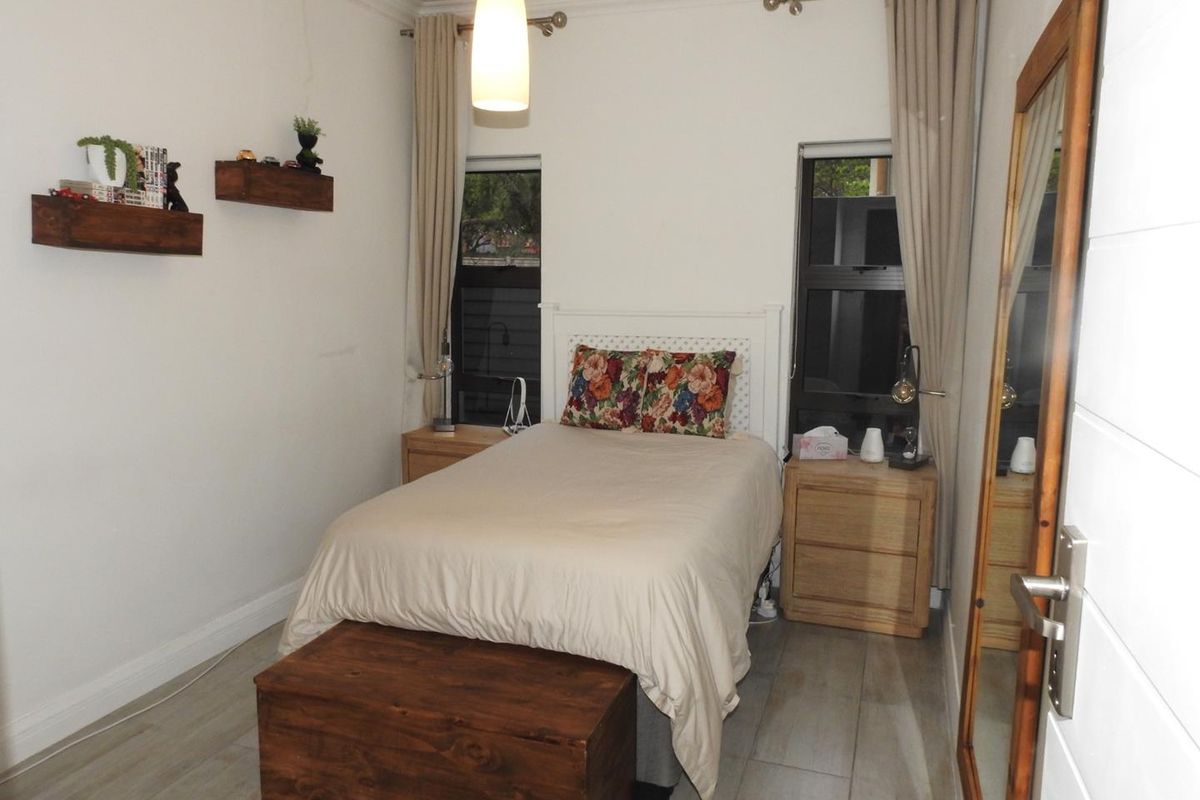 A well-maintained bedroom featuring laminate flooring, dual windows with curtain rods, and modern pendant lighting.