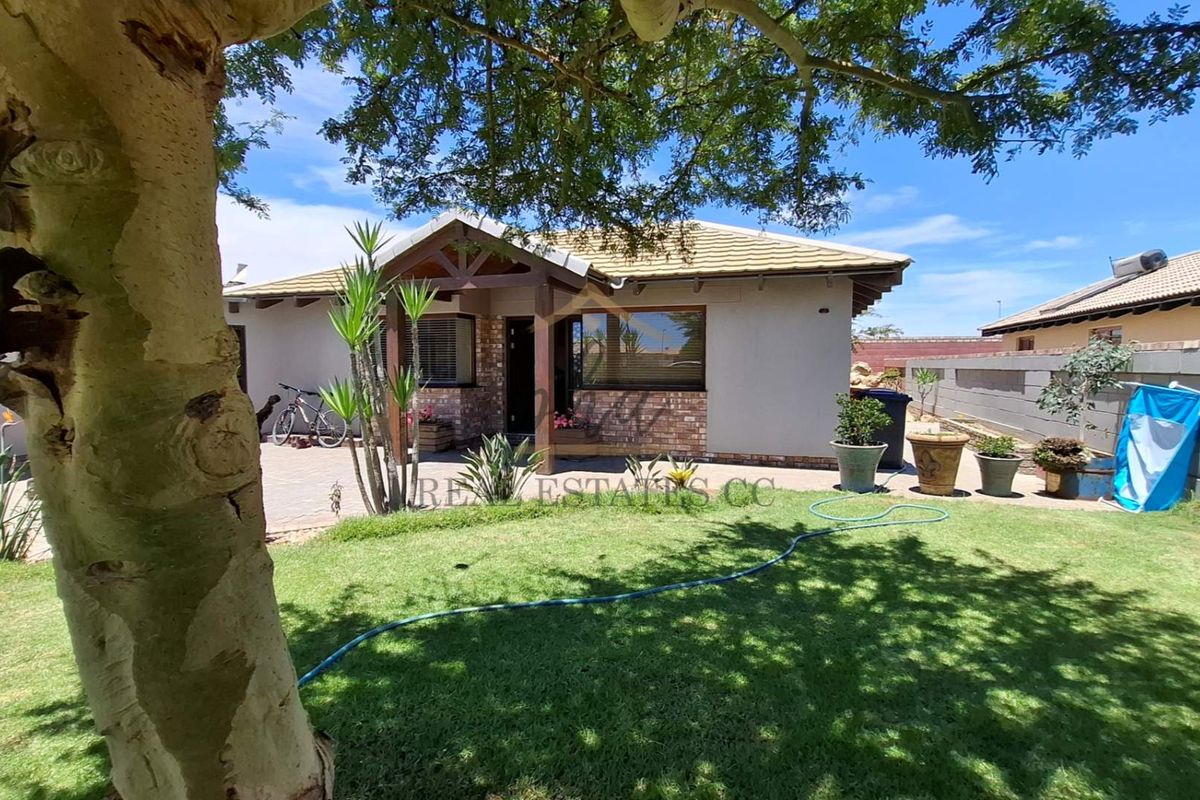 A view of the rear exterior of the house, featuring a paved patio area, a well-maintained lawn, and a perimeter boundary wall.