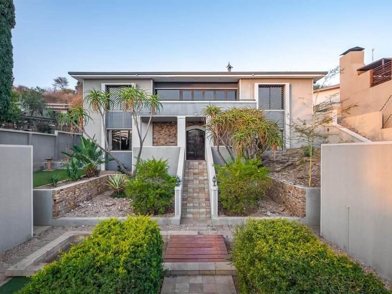 A well-maintained front facade featuring stone cladding, a paved entrance walkway with a timber bridge, and landscaped terraced garden beds.