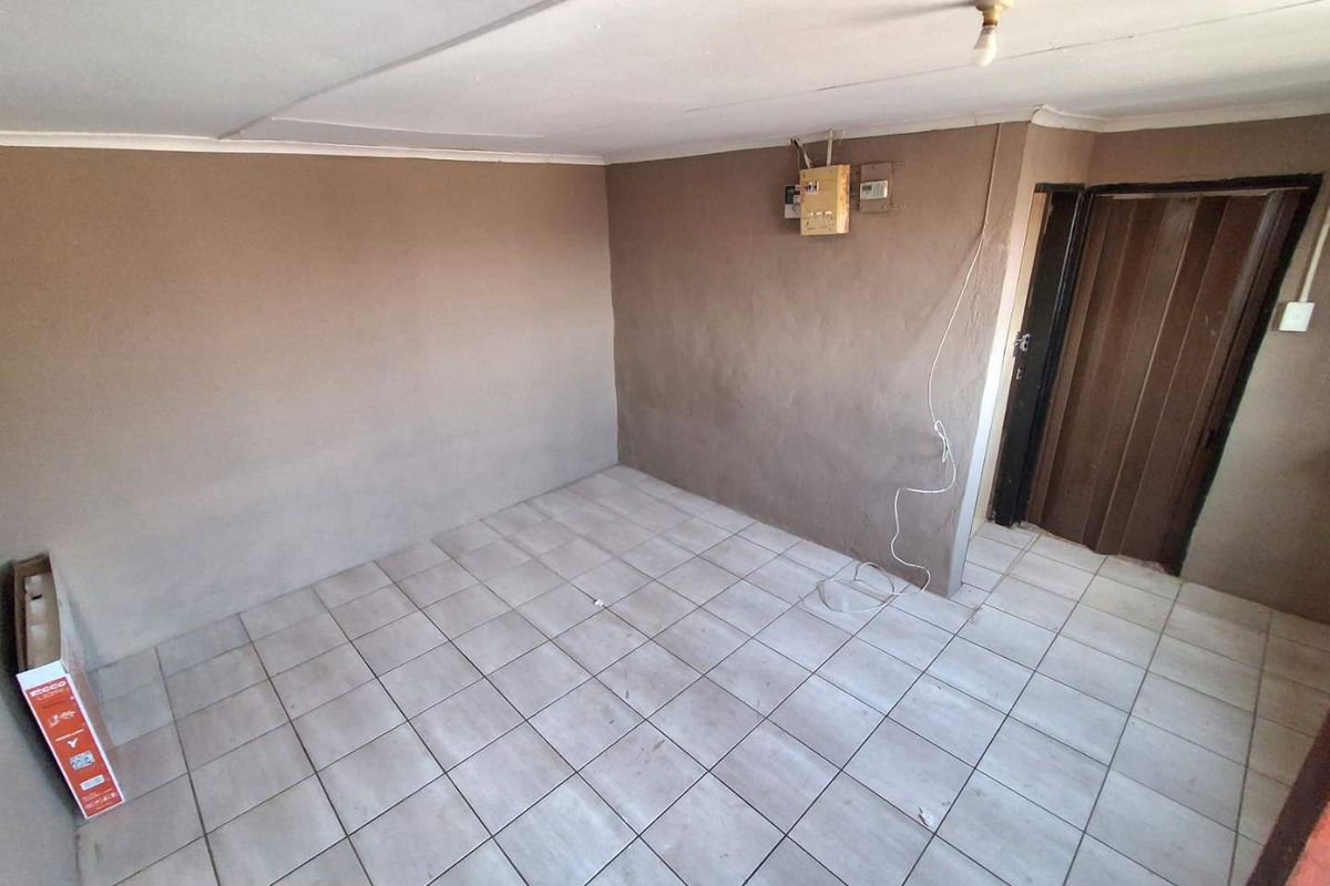An empty, unfinished living area featuring ceramic floor tiles, a folding door, and an exposed electrical distribution board.