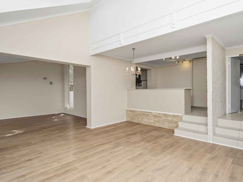 Spacious open-plan living area featuring vaulted ceilings, laminate flooring, and a stone feature wall with tiered levels leading to the kitchen and hallway.