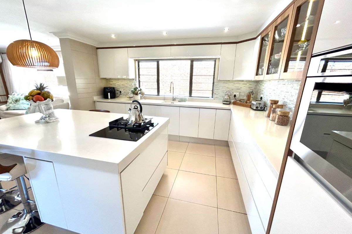 Modern kitchen featuring a large central island with a built-in gas hob, sleek white cabinetry, stone countertops, and tiled flooring.