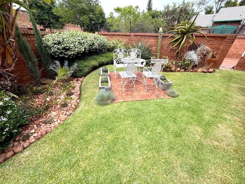 A well-maintained private garden featuring a brick paved seating area, lush lawn, and established perimeter brick boundary walls.