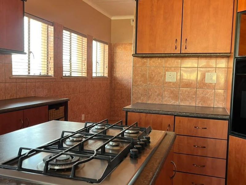 A functional kitchen featuring wood-finish cabinetry, laminate countertops, a built-in gas hob, and an integrated oven with tiled splashbacks.
