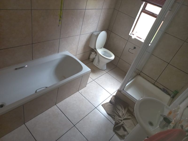 A functional bathroom featuring a bathtub, separate shower enclosure, toilet, and pedestal basin with neutral wall and floor tiling.