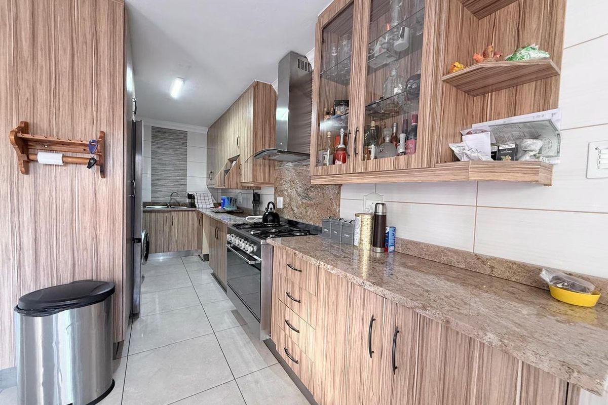 A functional kitchen featuring wood-grain cabinetry, granite countertops, a gas stove with extractor fan, and tiled flooring.