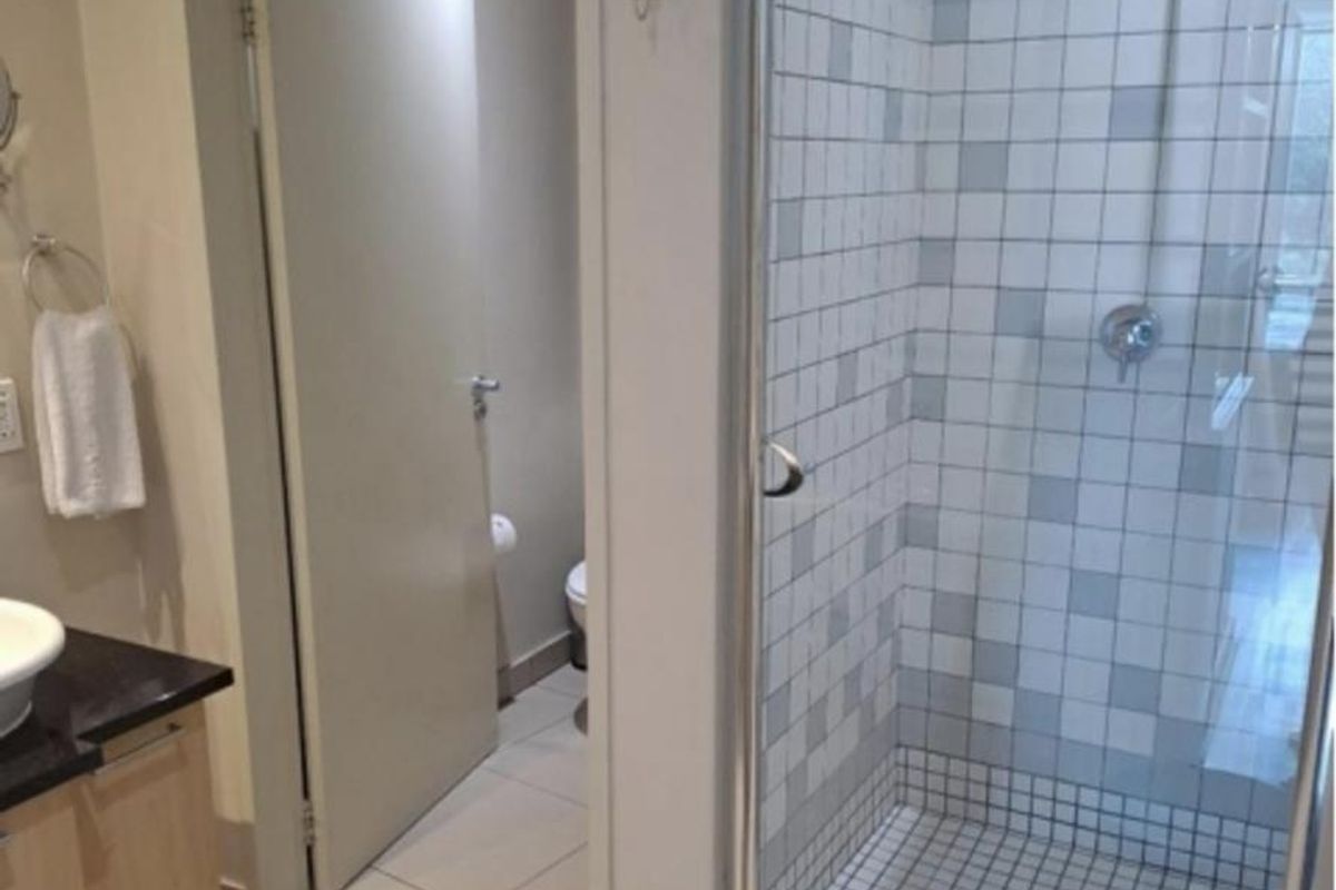 A functional bathroom featuring a glass-enclosed shower with mosaic tiling, a vanity with a dark countertop, and a separate toilet area.