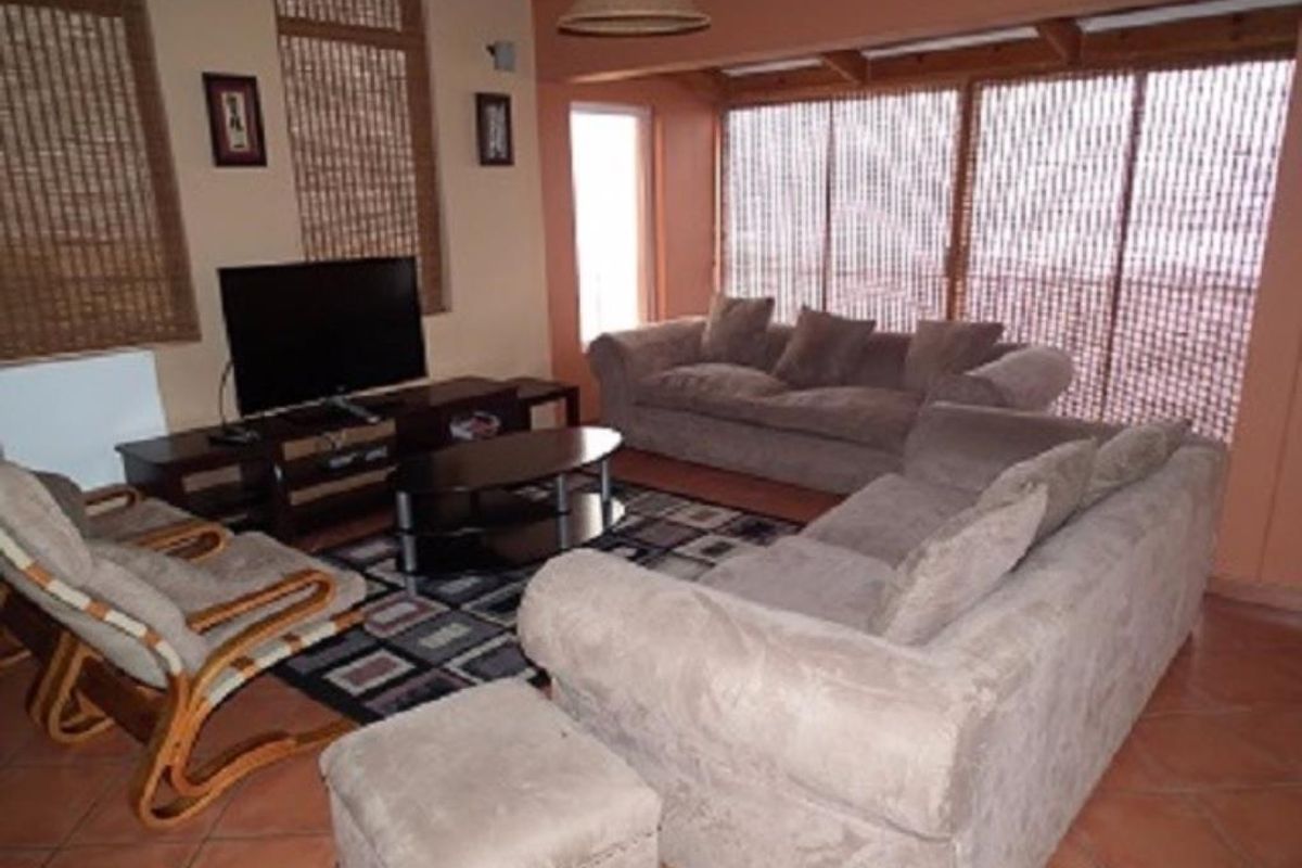 A comfortable living room featuring terracotta floor tiles, exposed timber ceiling beams, and large sliding glass doors that provide ample natural light.