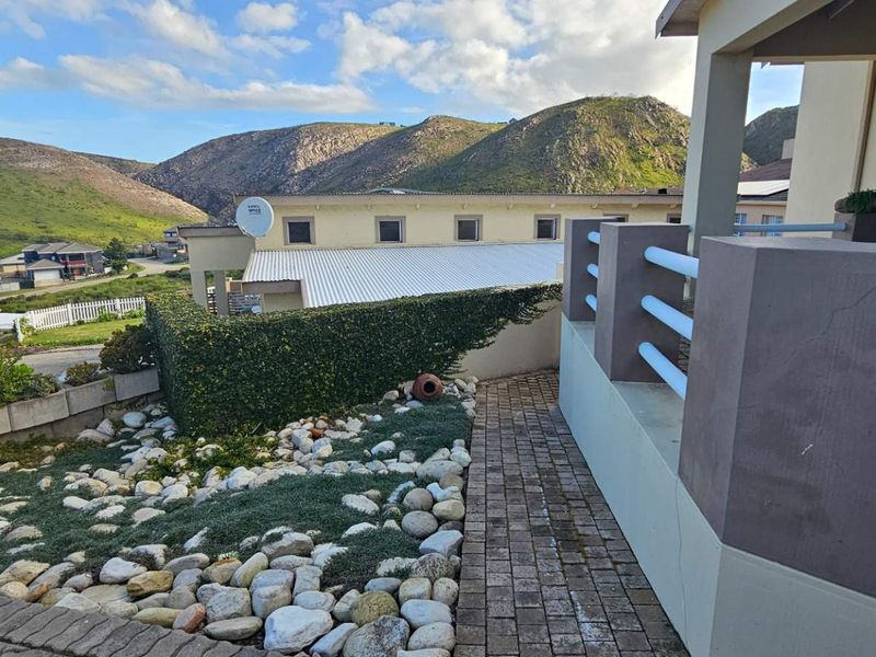 Rear exterior view of the property featuring a paved walkway, landscaped garden area, and a balustrade overlooking the surrounding estate and mountain landscape.