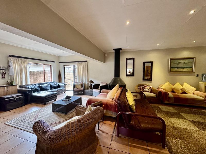 Spacious living room featuring tiled flooring, a central freestanding fireplace, and large windows providing natural light with access to the outdoor area.