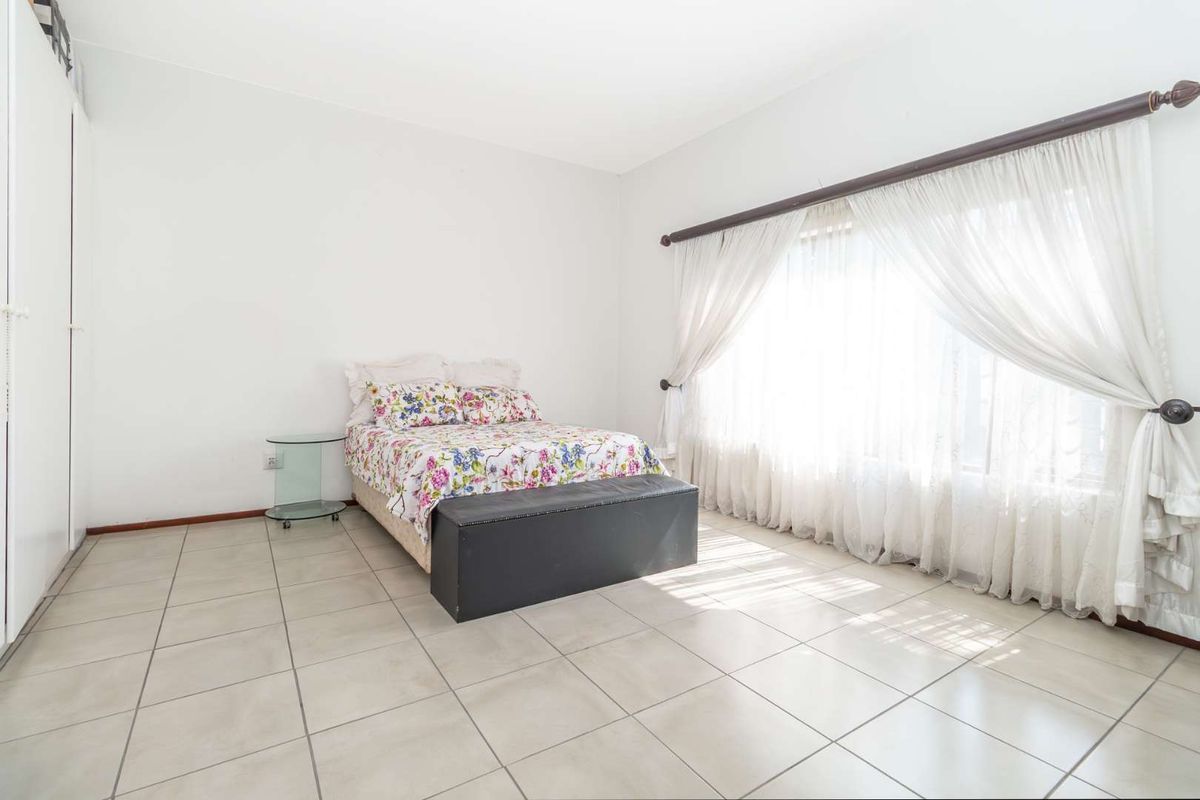 A bright bedroom featuring neutral floor tiles, built-in wardrobe storage, and large windows with curtain fixtures.