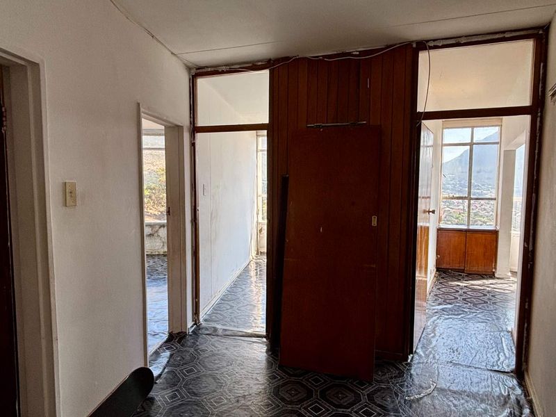 A vacant hallway featuring dated wood paneling, worn vinyl flooring, and multiple access points to adjacent rooms with natural light.
