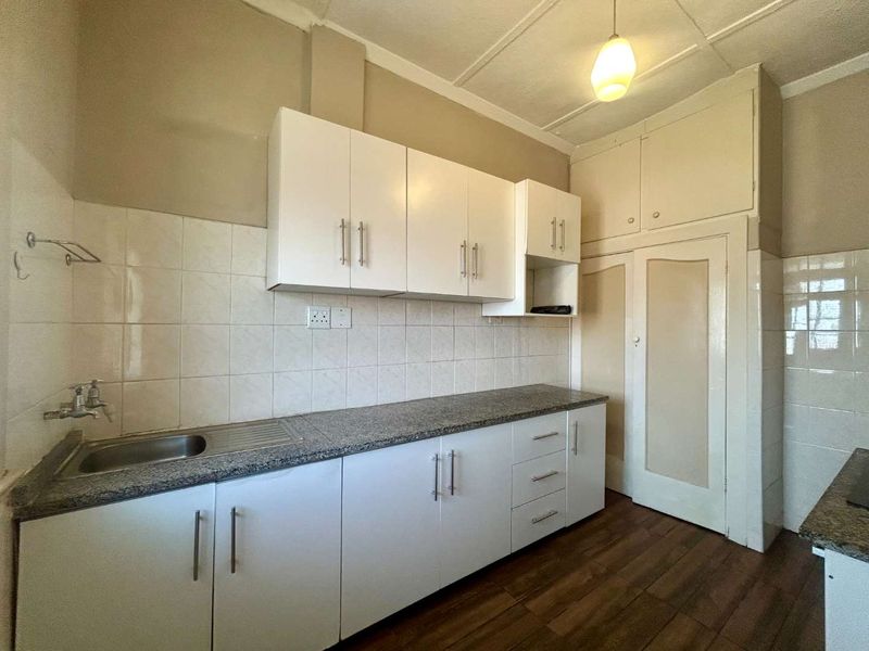 A functional kitchen featuring white built-in cabinetry, granite countertops, a stainless steel sink, and tiled backsplash with ample storage space.