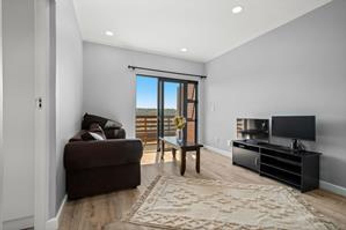 A bright living room featuring modern laminate flooring, recessed downlighting, and a sliding glass door providing access to an outdoor area.