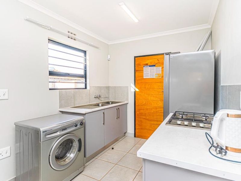 A functional scullery area featuring built-in cabinetry, a stainless steel sink, tiled splashbacks, and a built-in gas hob.