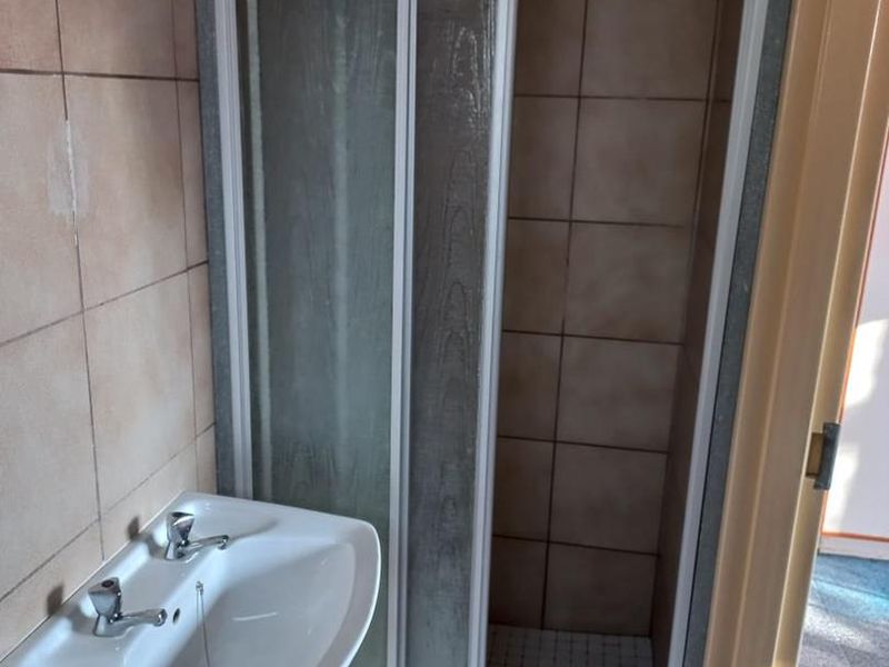 A compact bathroom featuring a shower enclosure and a wall-mounted basin with tiled finishes, requiring some cosmetic maintenance.